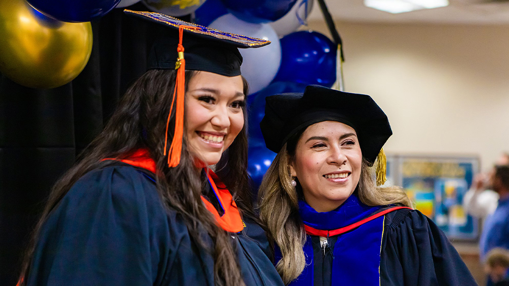 A student stands with the Dean of the College of Engineering in graduation attire.