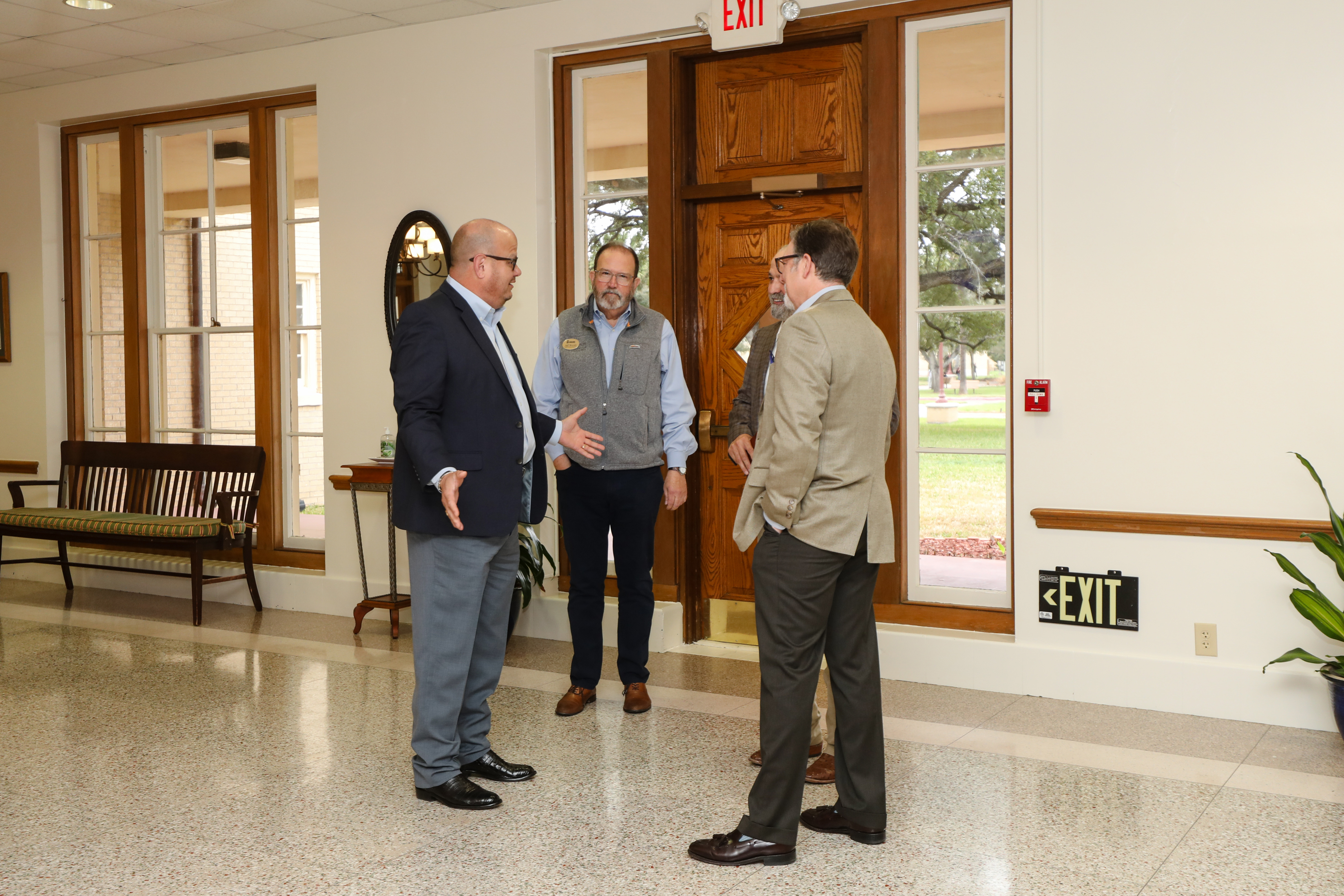 Three people having a discussion in front of one of the exits of the Founders Room.